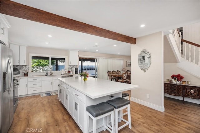 kitchen with stainless steel fridge with ice dispenser, light wood-style floors, a sink, beamed ceiling, and a kitchen bar