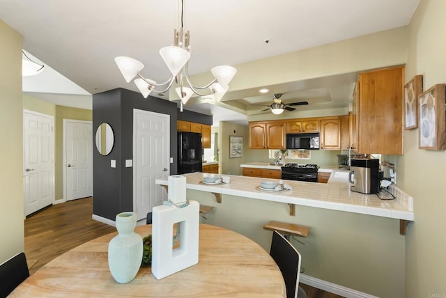 kitchen with pendant lighting, brown cabinets, a raised ceiling, a peninsula, and black appliances