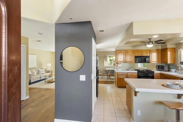 kitchen featuring light tile patterned floors, visible vents, tile countertops, black appliances, and a kitchen bar