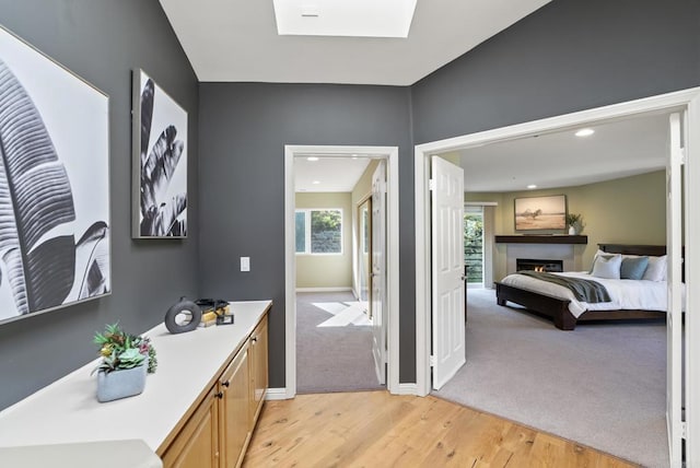 bathroom featuring a skylight, a warm lit fireplace, baseboards, wood finished floors, and recessed lighting