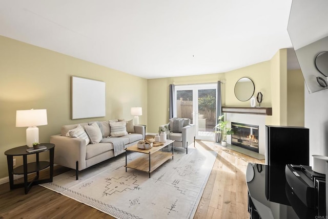 living room featuring light wood-type flooring, a glass covered fireplace, and baseboards