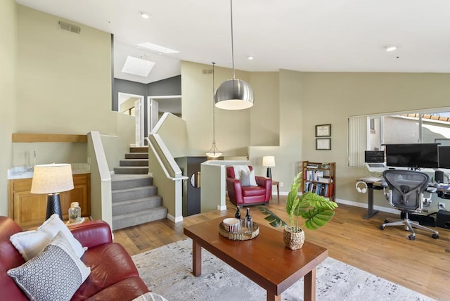 living area featuring stairs, vaulted ceiling with skylight, light wood-type flooring, and visible vents