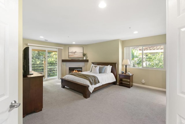 bedroom with access to exterior, light colored carpet, a lit fireplace, and multiple windows