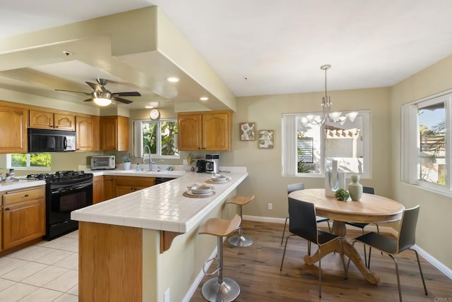 kitchen featuring black appliances, hanging light fixtures, a breakfast bar area, and baseboards