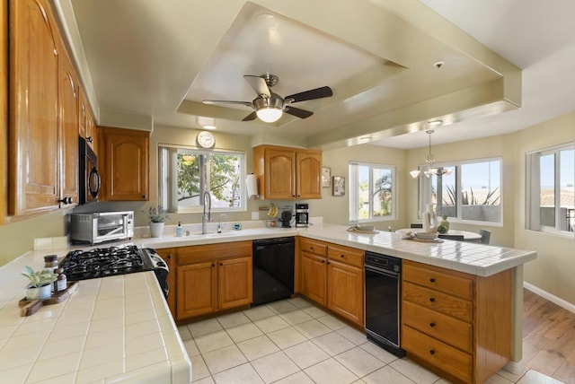 kitchen with a peninsula, a tray ceiling, black appliances, pendant lighting, and a sink