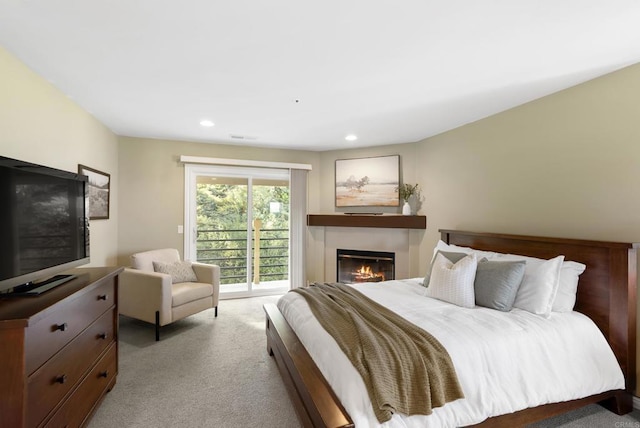 bedroom with light carpet, access to outside, recessed lighting, and a glass covered fireplace