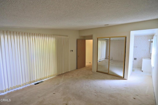 unfurnished bedroom featuring visible vents, ensuite bathroom, carpet, a textured ceiling, and a closet