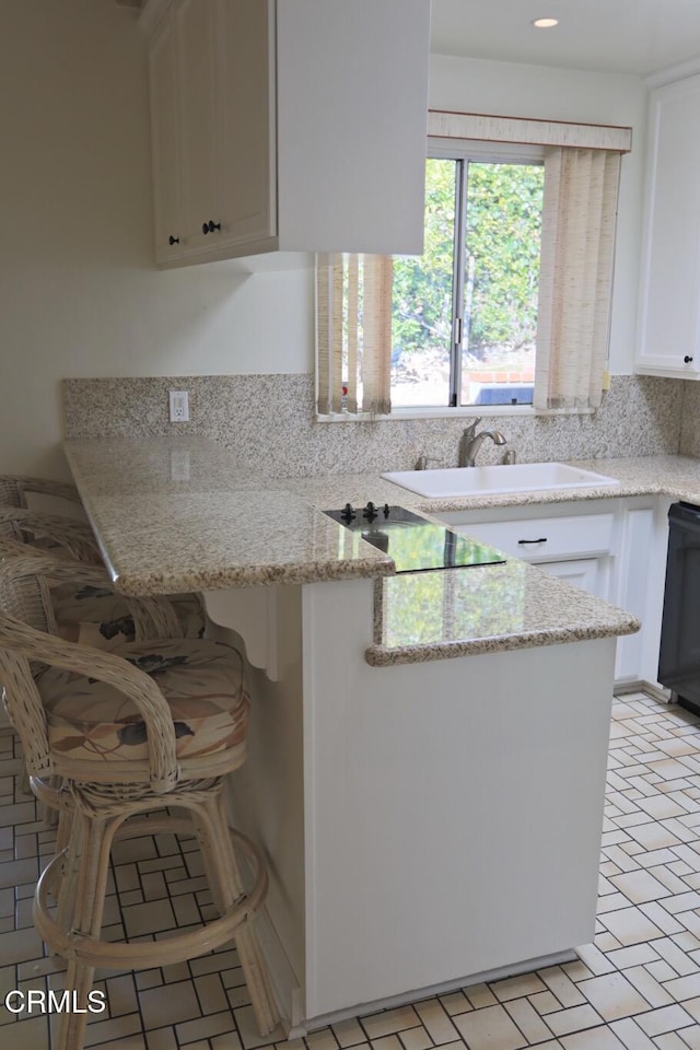 kitchen with black appliances, white cabinetry, light stone counters, and a sink