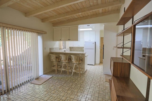 kitchen featuring a peninsula, white cabinetry, light countertops, freestanding refrigerator, and a kitchen bar