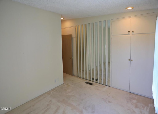 interior space with a textured ceiling, recessed lighting, visible vents, and light colored carpet