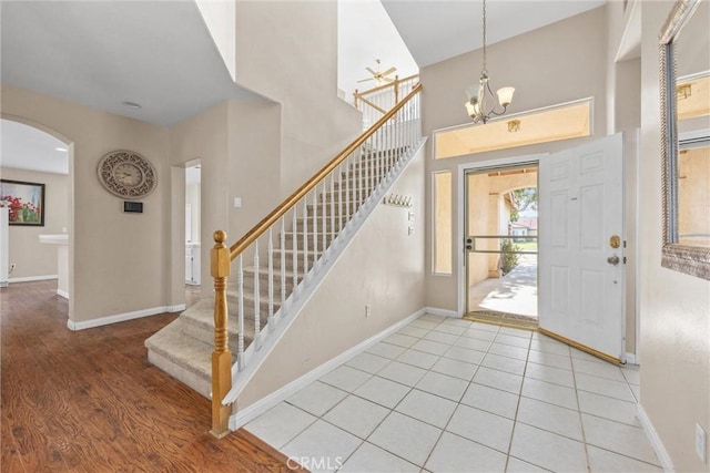 entryway featuring baseboards, arched walkways, light wood-style flooring, stairway, and a notable chandelier