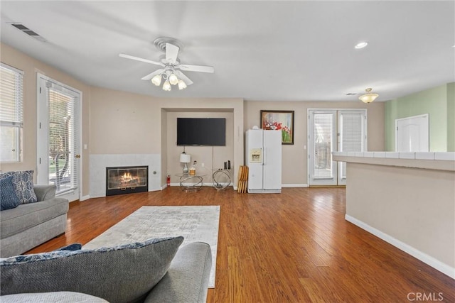 living room featuring visible vents, a tiled fireplace, ceiling fan, wood finished floors, and baseboards