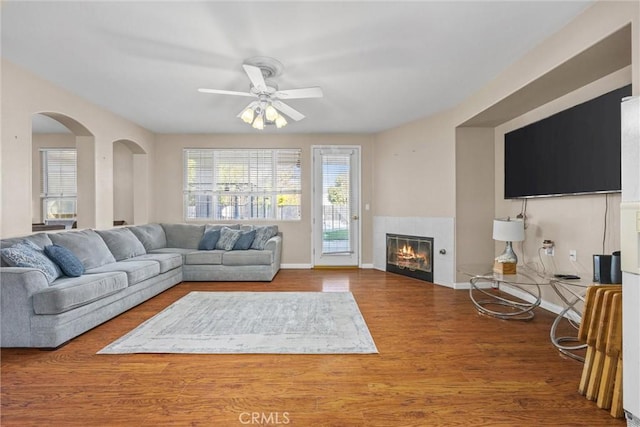 living area with a ceiling fan, baseboards, a tiled fireplace, and wood finished floors