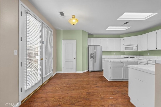 kitchen with white appliances, a skylight, tile counters, white cabinets, and dark wood-style flooring