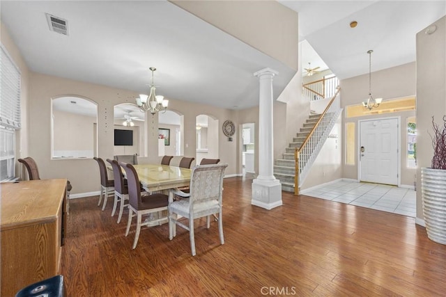 dining area with ceiling fan with notable chandelier, visible vents, stairway, light wood-type flooring, and decorative columns