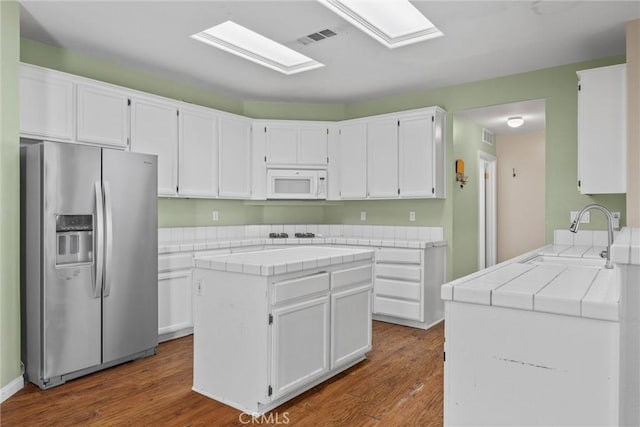 kitchen featuring white microwave, a kitchen island, white cabinetry, and stainless steel refrigerator with ice dispenser