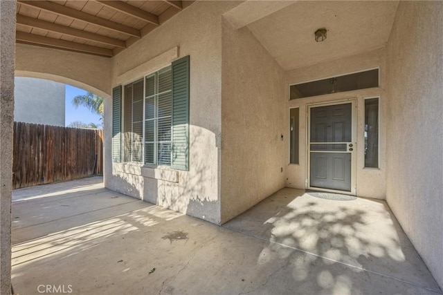 entrance to property featuring a patio area, fence, and stucco siding