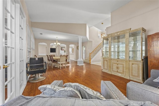 living area featuring decorative columns, arched walkways, lofted ceiling, wood finished floors, and a chandelier