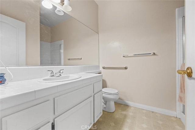 bathroom with toilet, vanity, baseboards, and walk in shower