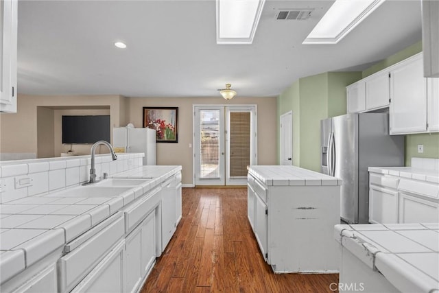 kitchen featuring white appliances, white cabinetry, visible vents, and tile counters