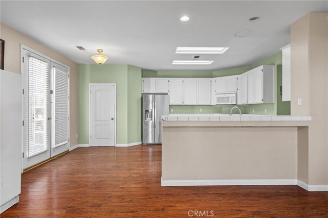 kitchen with tile countertops, white microwave, a skylight, white cabinetry, and stainless steel refrigerator with ice dispenser