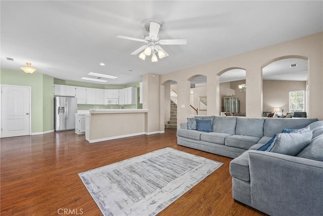 living area featuring baseboards, visible vents, ceiling fan, dark wood-style flooring, and stairs