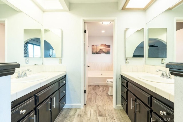 full bath featuring a garden tub, two vanities, a sink, and wood finished floors