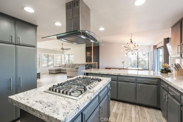 kitchen featuring a kitchen island, open floor plan, gray cabinets, island exhaust hood, and stainless steel gas stovetop