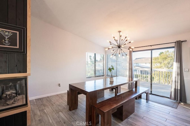 dining area with lofted ceiling, a notable chandelier, a large fireplace, wood finished floors, and baseboards