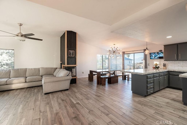 living area with lofted ceiling, ceiling fan with notable chandelier, baseboards, and light wood-style floors