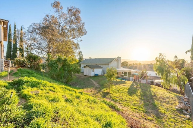 yard at dusk with a storage shed, an outbuilding, fence, and a pergola