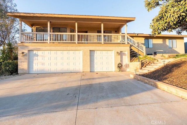 front of property with stucco siding, stairway, an attached garage, a balcony, and driveway