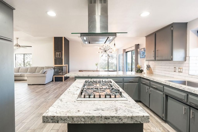 kitchen with open floor plan, island exhaust hood, gray cabinets, light countertops, and stainless steel gas stovetop