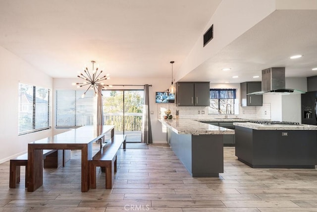 kitchen with pendant lighting, extractor fan, a peninsula, light wood finished floors, and tasteful backsplash