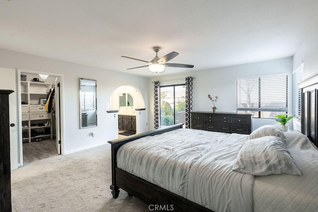 carpeted bedroom featuring connected bathroom, a spacious closet, baseboards, and a ceiling fan