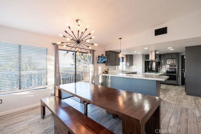 dining space featuring light wood-type flooring, lofted ceiling, visible vents, and a notable chandelier