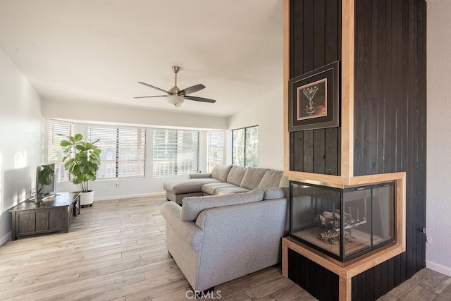 living room featuring light wood-type flooring, a multi sided fireplace, ceiling fan, and baseboards