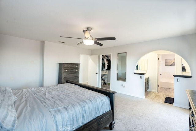 bedroom featuring light carpet, baseboards, visible vents, arched walkways, and a walk in closet