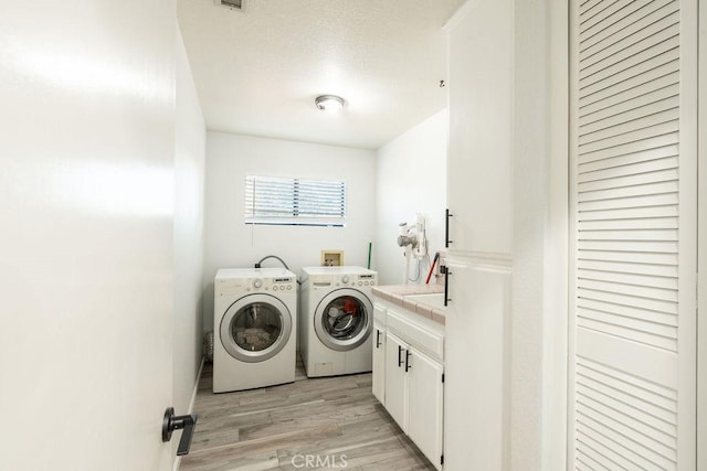 laundry room with cabinet space, light wood finished floors, visible vents, washing machine and clothes dryer, and a sink