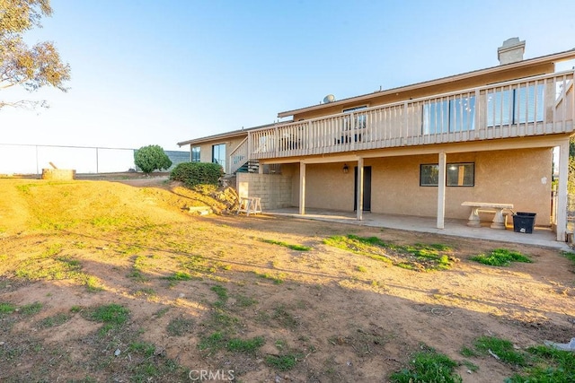 rear view of house with fence, a wooden deck, and stucco siding