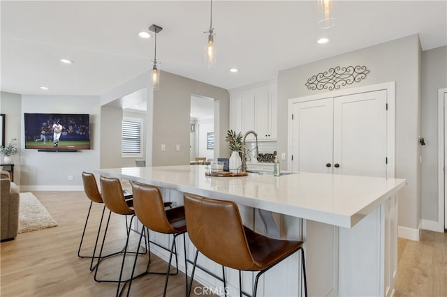 kitchen with a spacious island, light wood-style flooring, a breakfast bar, hanging light fixtures, and white cabinetry