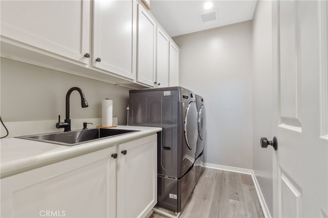 clothes washing area with light wood finished floors, cabinet space, visible vents, a sink, and washer and dryer