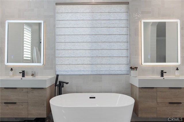 bathroom with a freestanding tub, two vanities, a sink, and tile walls