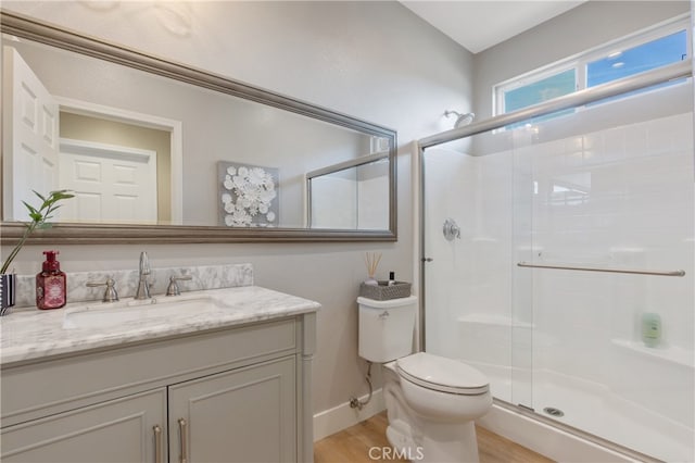 bathroom featuring baseboards, toilet, wood finished floors, vanity, and a shower stall