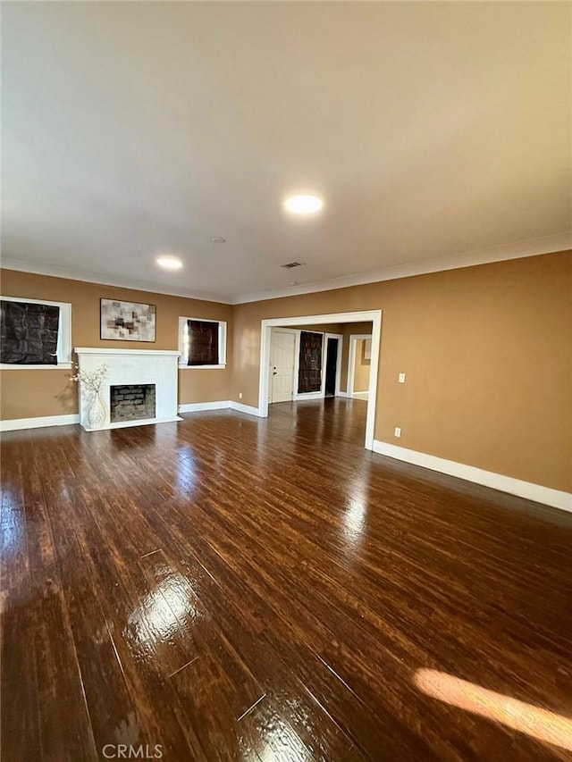 unfurnished living room with dark wood-style floors, a fireplace, baseboards, and ornamental molding