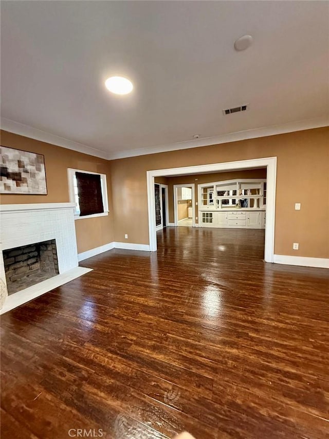 unfurnished living room with crown molding, dark wood finished floors, a fireplace, visible vents, and baseboards