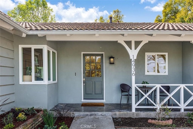 entrance to property featuring covered porch, a tiled roof, and stucco siding