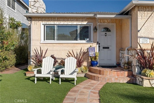 view of exterior entry featuring a yard, a chimney, and stucco siding