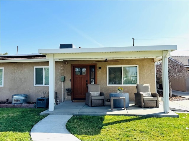 rear view of property featuring a yard, roof mounted solar panels, a patio, and stucco siding