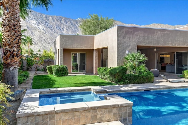 back of property featuring stucco siding, a lawn, a mountain view, an in ground hot tub, and an outdoor pool